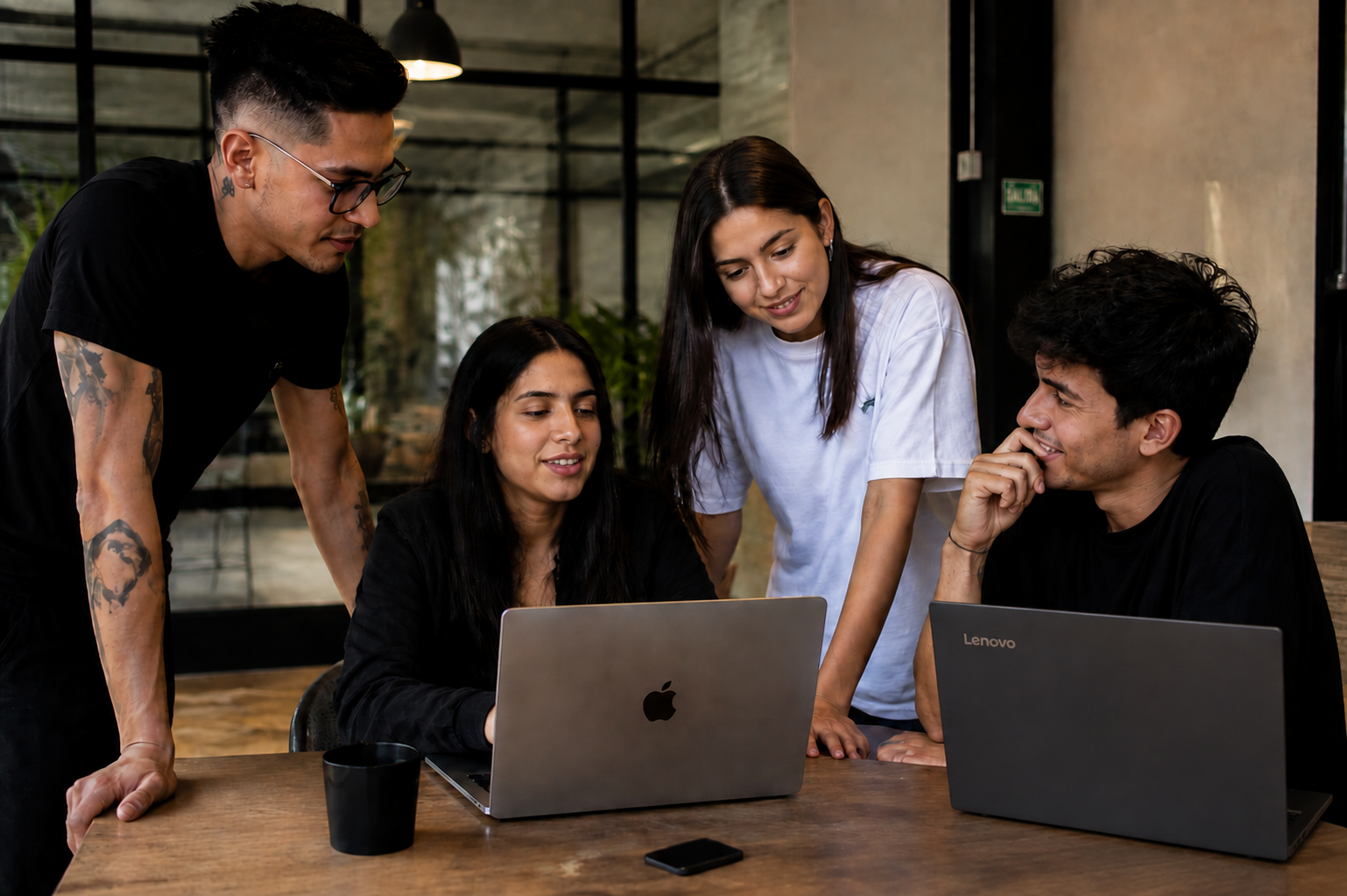 Cuatro jóvenes profesionales conversando alrededor de una laptop en un espacio de coworking